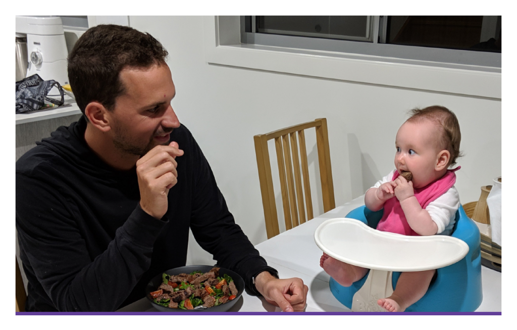 Baby eating meat with father.