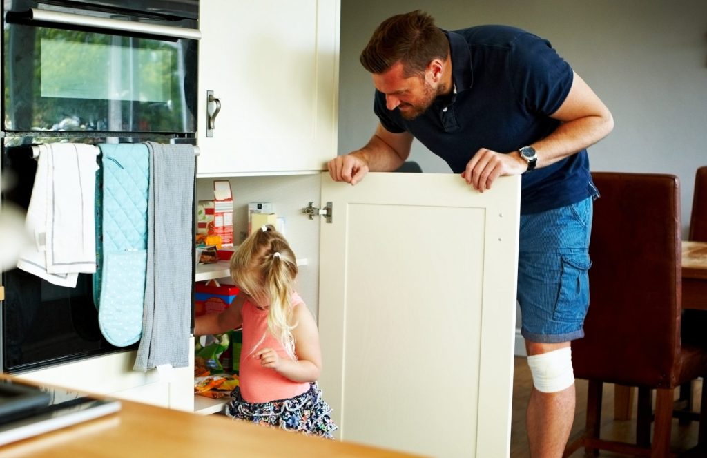 Girl looking in cupboard for food with dad looking on
