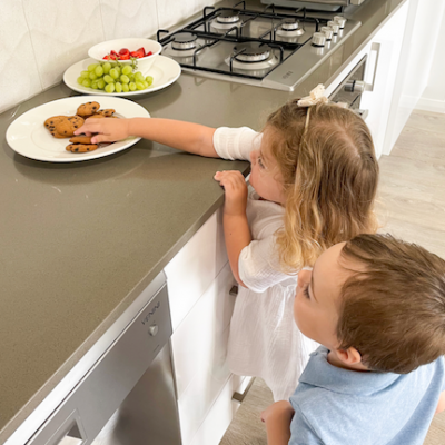 young girl reaching for cookies on top of kitchen bench with young boy looking over her shoulder