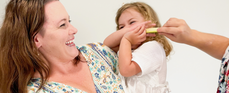 Mother trying to force child to eat zucchini, mother holding child smiling