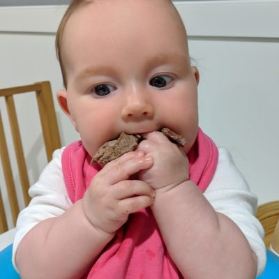 Baby putting meat in mouth.
