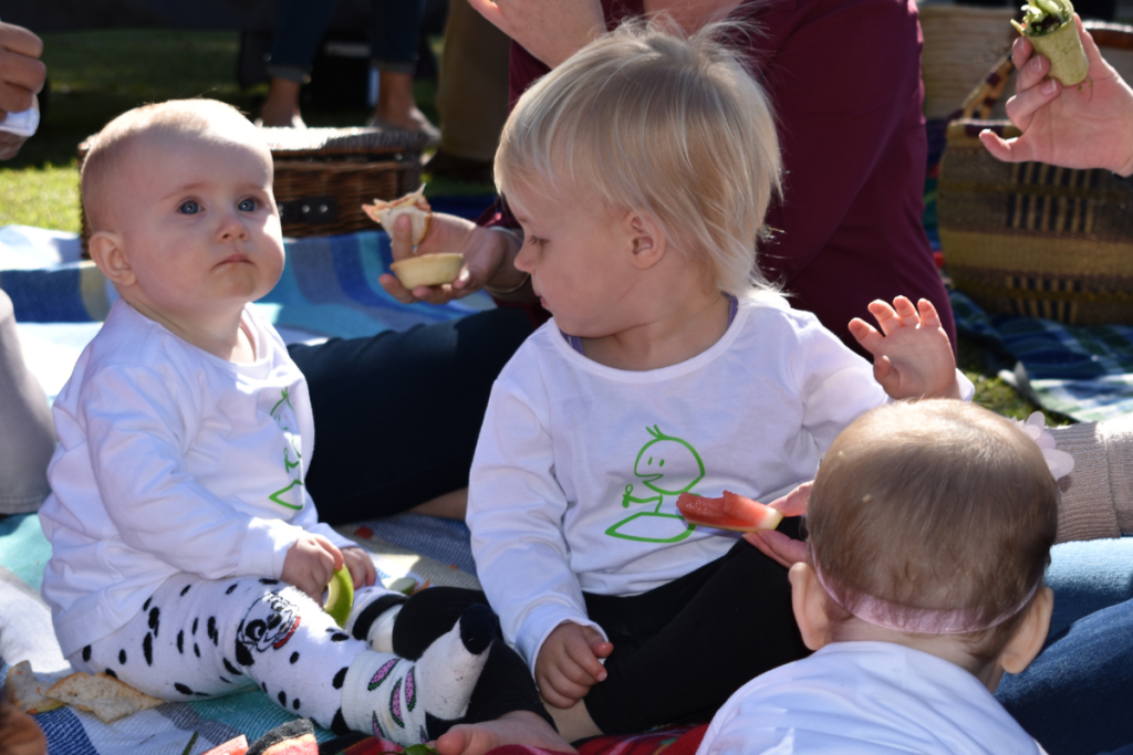 Children sitting on rug at picnic.